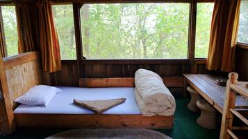 Una habitación de cabaña de madera con una cama, una mesa y vistas a los árboles por la ventana.