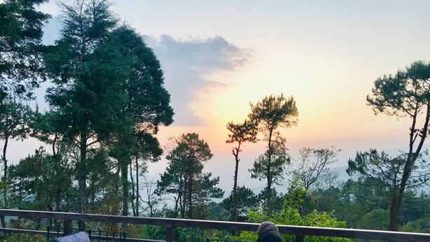 Un balcone con posti a sedere all'aperto e vista su alberi e un tramonto.