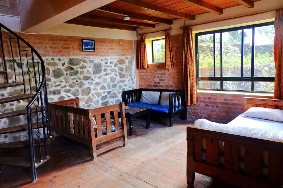 A room with a stone wall, wooden staircase, a bed, a sofa, and a window with curtains.