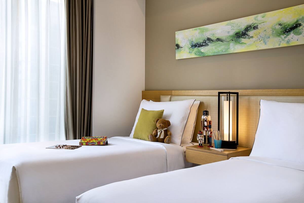A hotel room with two beds, a nightstand, a lamp, and a painting on the wall.
