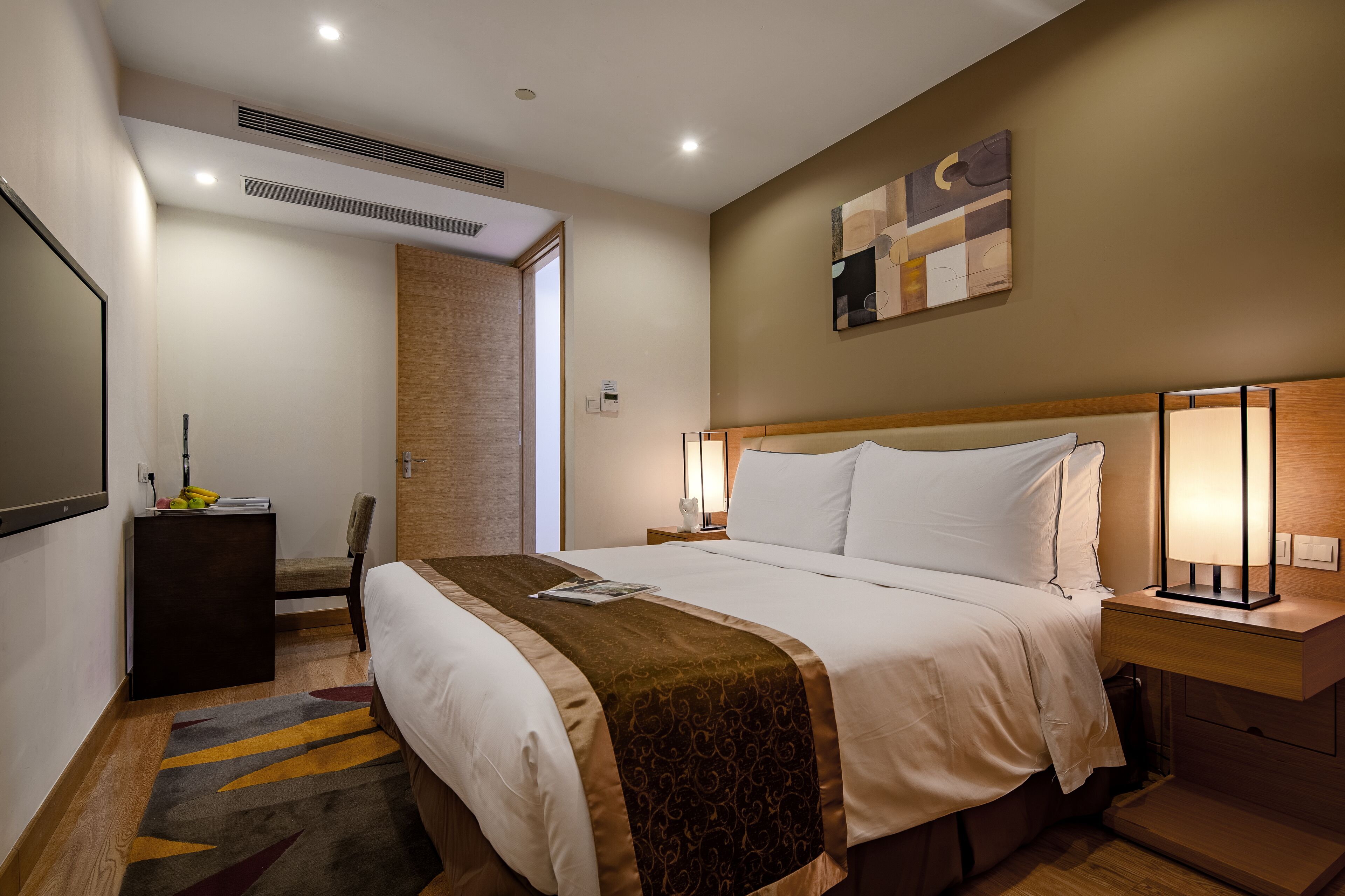 Una habitación de hotel con una cama grande, lámparas de noche, un escritorio pequeño y una obra de arte colgada en la pared.