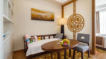 A hotel room with a bed, a dining table with a fruit plate, a lamp, and a decorative wall piece.