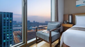 Une chambre d’hôtel dotée d’une grande fenêtre donnant sur la ville, d’un lit, d’une chaise et d’une table de chevet.
