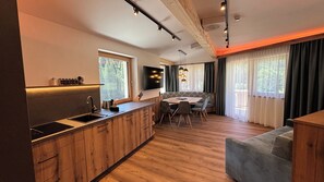 A modern kitchen with wooden cabinetry, a dining area with a round table, and a seating arrangement. - Anja's Schönblick - Bed & Breakfast (Gerlos)