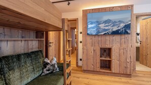 A wooden interior with a green sofa, wooden shelves, and a large framed picture of mountains.