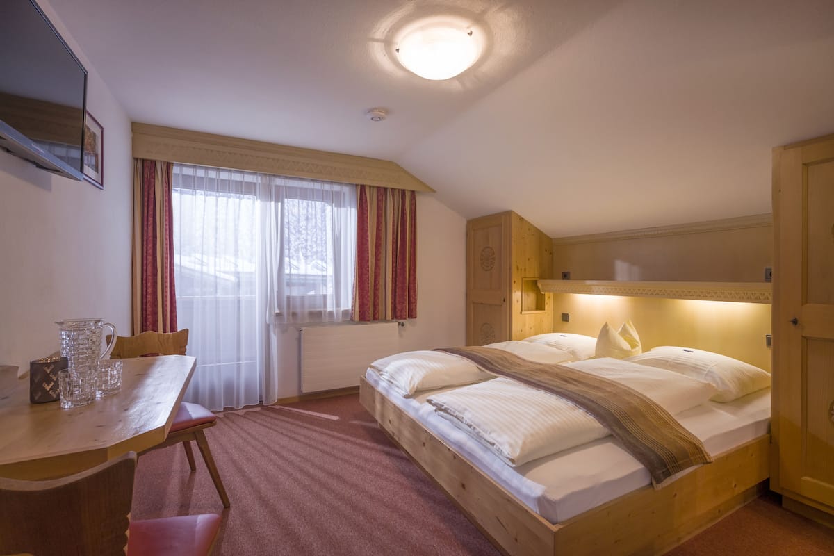 Un dormitorio con cama de madera, un escritorio con silla, un radiador y una ventana con cortinas.