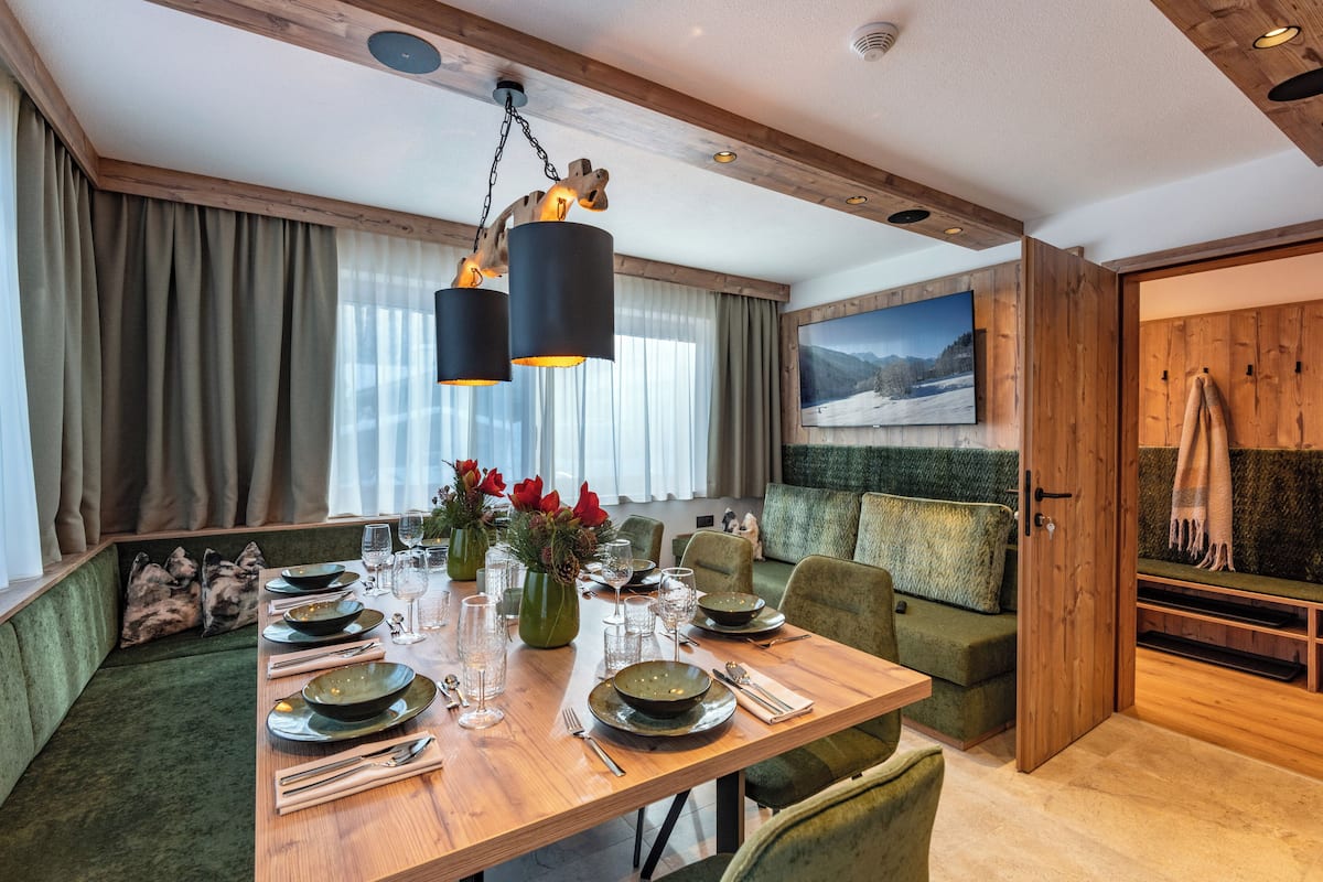 Un comedor con una mesa de madera preparada para cuatro personas, rodeada de asientos tapizados en tono verde.
