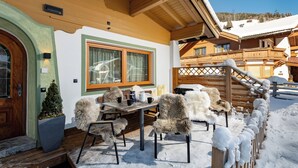 A wooden chalet with a snow-covered porch, a wooden staircase, and a view of the surrounding snowy landscape.