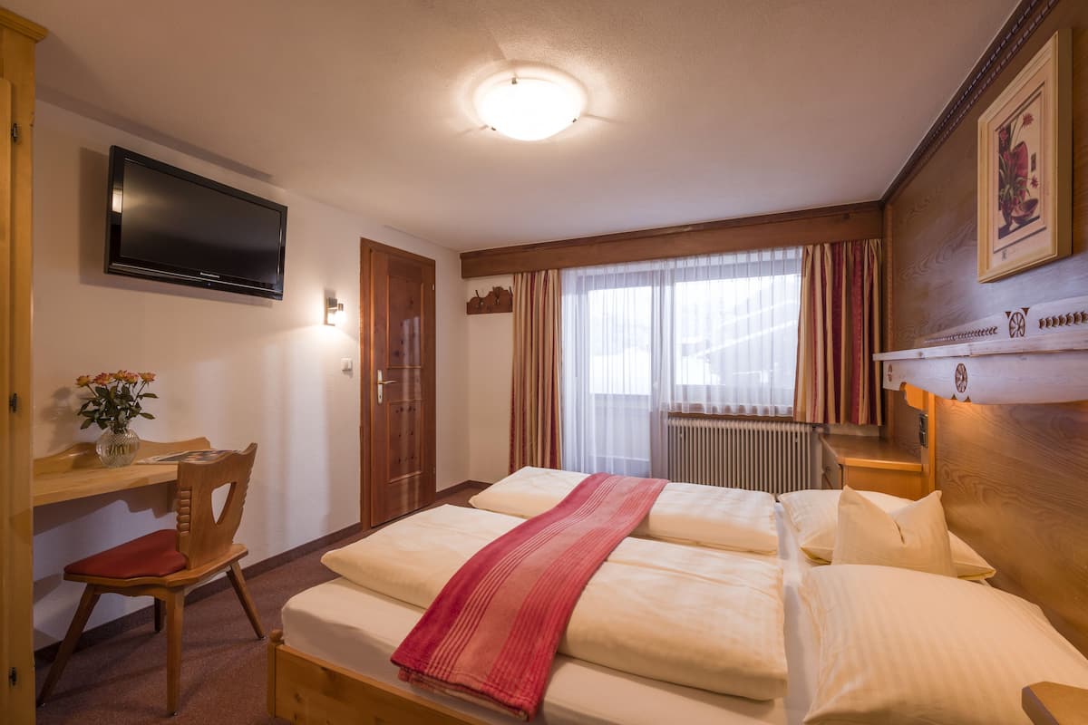 Habitación de hotel con cama, escritorio, silla, televisor y ventana con cortinas.