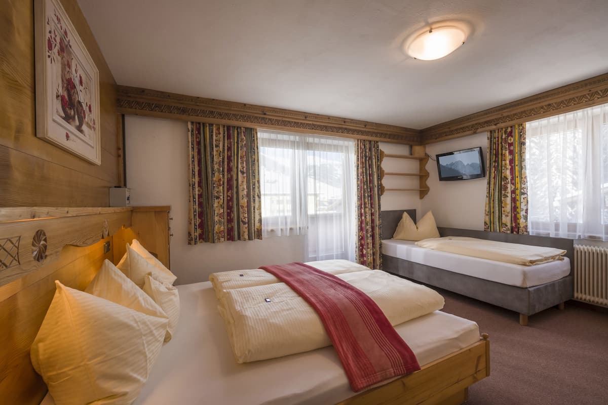 Un dormitorio con dos camas, cabeceros de madera, un televisor y cortinas estampadas.