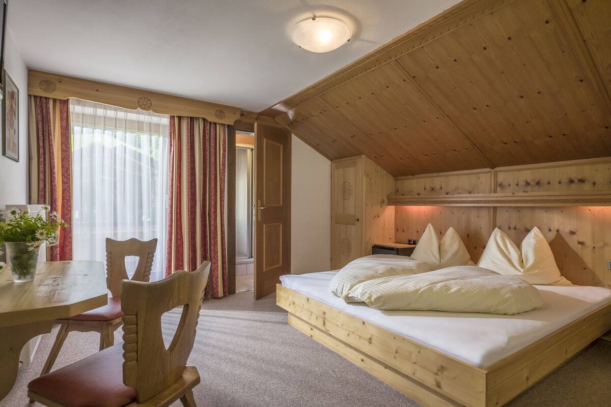 Una habitación de madera con una cama, una mesa de comedor, sillas y una ventana con cortinas.