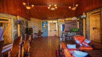 A spacious room with wooden floors and walls, a chandelier, and several wooden chairs and tables.