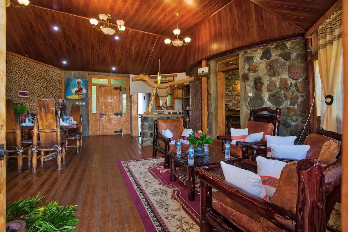 A spacious room with wooden flooring, a stone wall, and a dining area with wooden furniture.