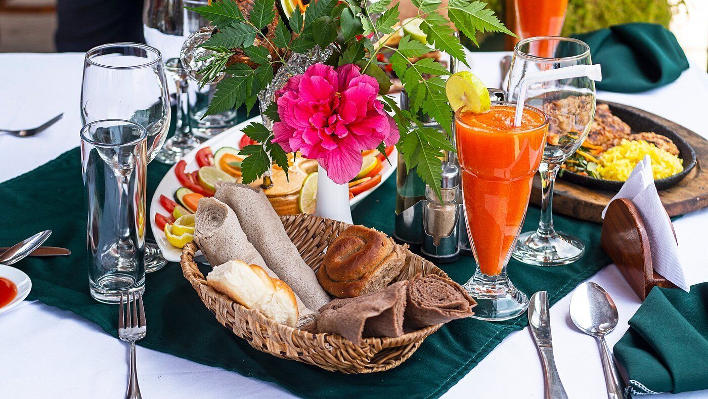 A table set with a variety of foods including bread, a salad, and a glass of juice, with a decorative flower centerpiece.