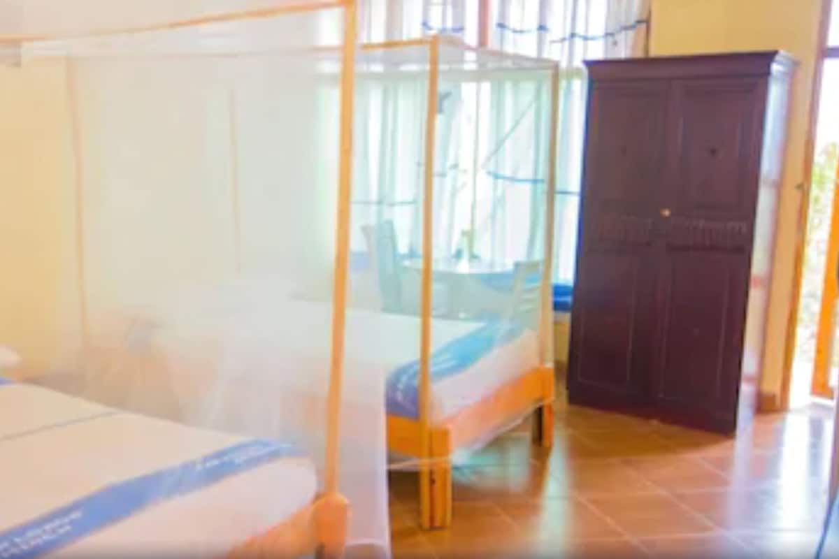 A room with two beds, each with a canopy. There is a wooden wardrobe and a window with curtains.