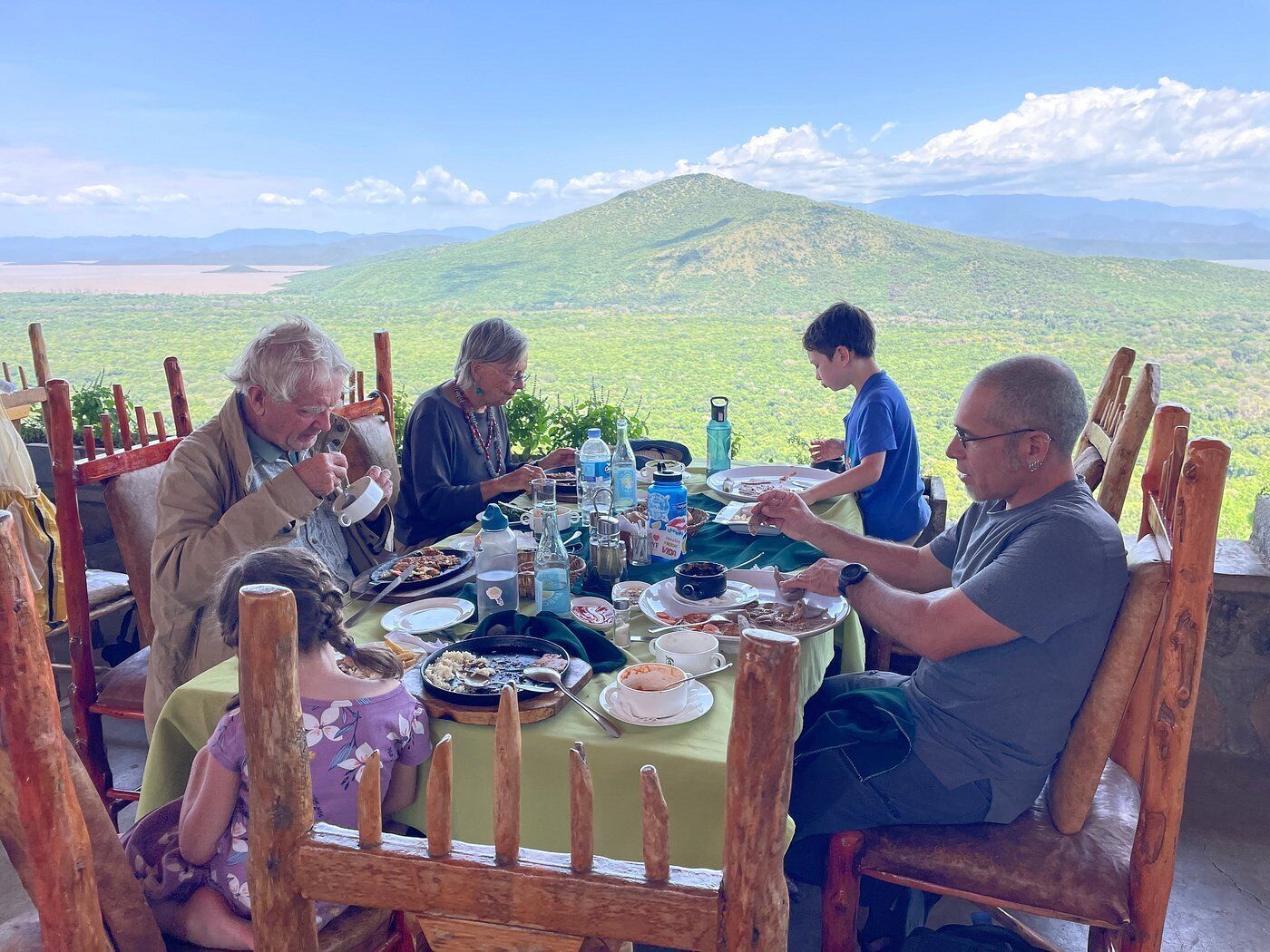 A group of people dining at an outdoor table with a scenic mountain view in the background.