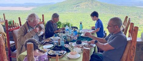 A group of people dining at an outdoor table with a scenic mountain view in the background.