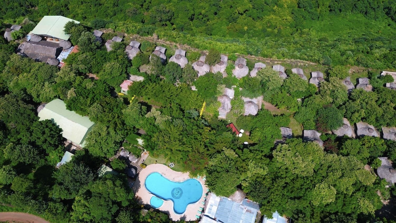 Vista aérea de una propiedad con piscina, varias edificaciones y un bosque denso que rodea la zona.