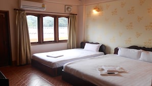 Habitación de hotel con dos camas, una ventana con cortinas, un equipo de aire acondicionado y una pared con estampado floral.