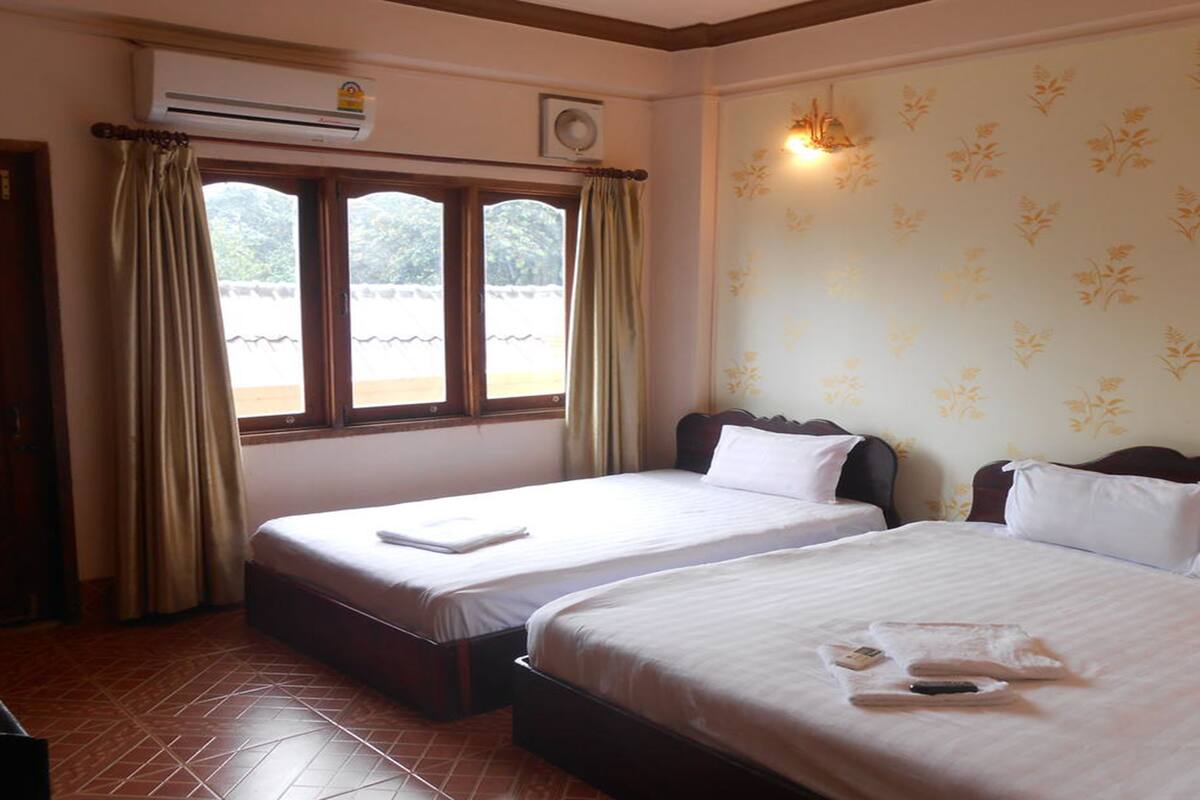Habitación de hotel con dos camas, una ventana con cortinas, un equipo de aire acondicionado y una pared con estampado floral.