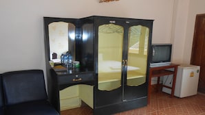 Una habitación con un armario negro, un televisor pequeño sobre un soporte de madera y un refrigerador.