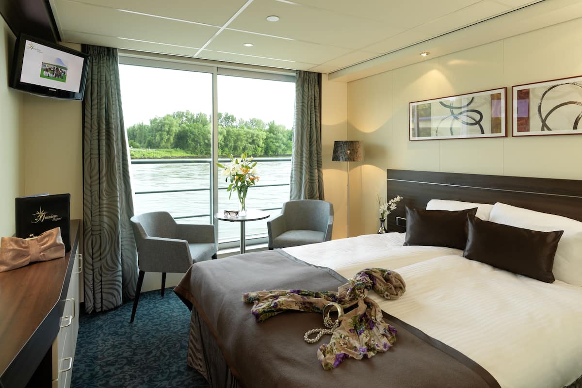 Ein Hotelzimmer mit einem großen Bett, zwei Sesseln, einem Schreibtisch und Blick auf einen Fluss.