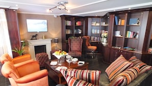 A living room with a sofa, armchairs, a coffee table, and a fireplace. There is a bookshelf filled with books and a television mounted on the wall. - Crossgates Hotelship AltstadtNord - Köln (Cologne)