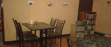 A dining area with a wooden table and chairs, a bookshelf, and a clock on the wall.