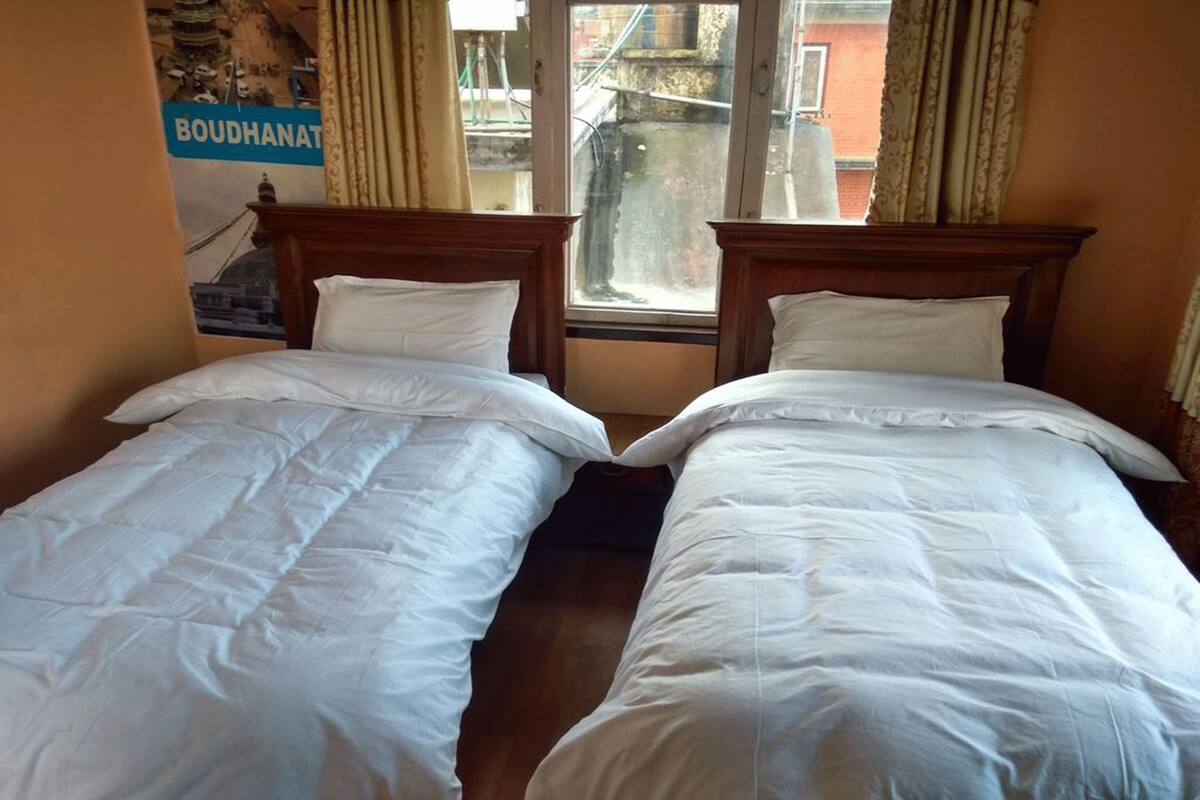 Two single beds with wooden headboards and white bedding in a room with a window and a poster on the wall.