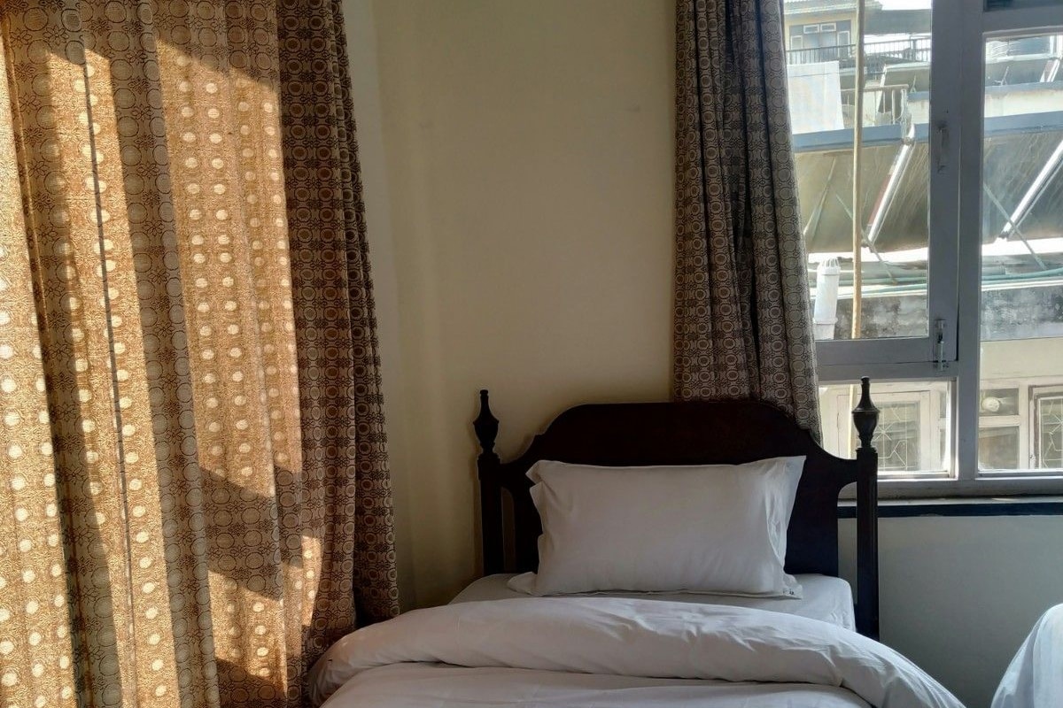 A single bed with white bedding in a room with a window and patterned curtains.