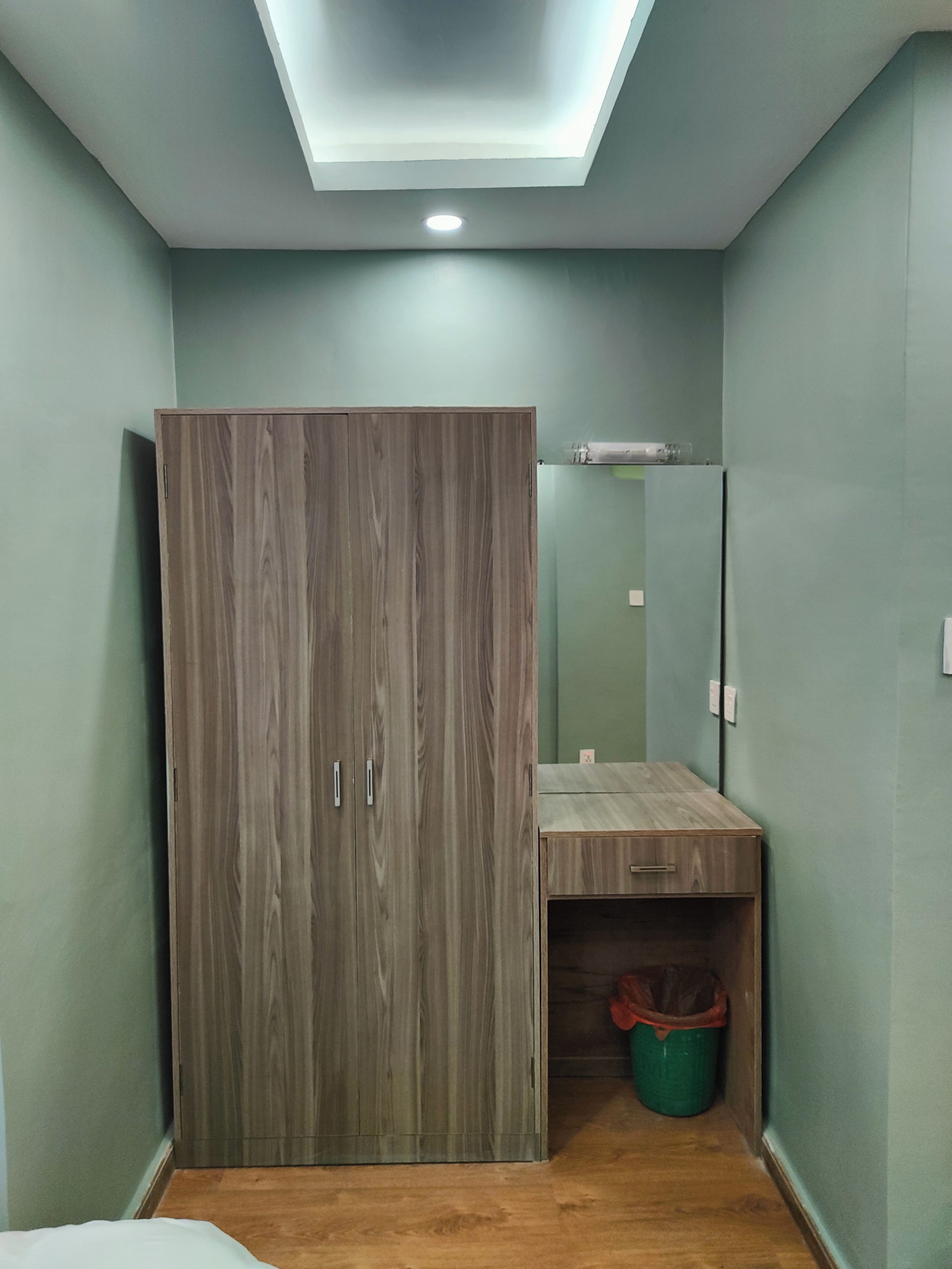 Une chambre avec une armoire, un miroir, un petit bureau et une poubelle.