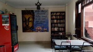 Une pièce décorée d’une fresque représentant Bouddha, avec une bibliothèque, un réfrigérateur Coca-Cola et une table entourée de chaises.