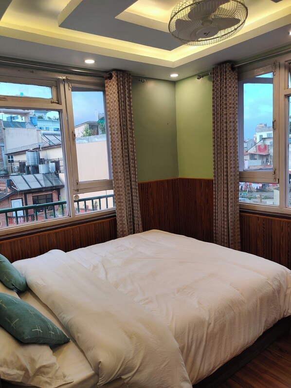 A bedroom with a large bed, wooden paneling, patterned curtains, and a view of buildings outside. - Family Peace House (Kathmandu)