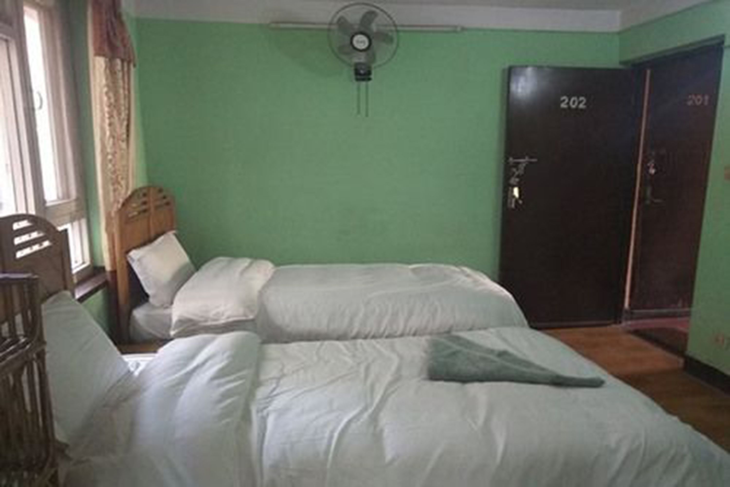 A room with two beds, a fan, and a door labeled 202.