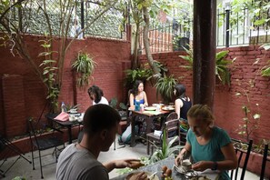 An outdoor dining area with brick walls, potted plants, and tables. - Family Peace House (Kathmandu)