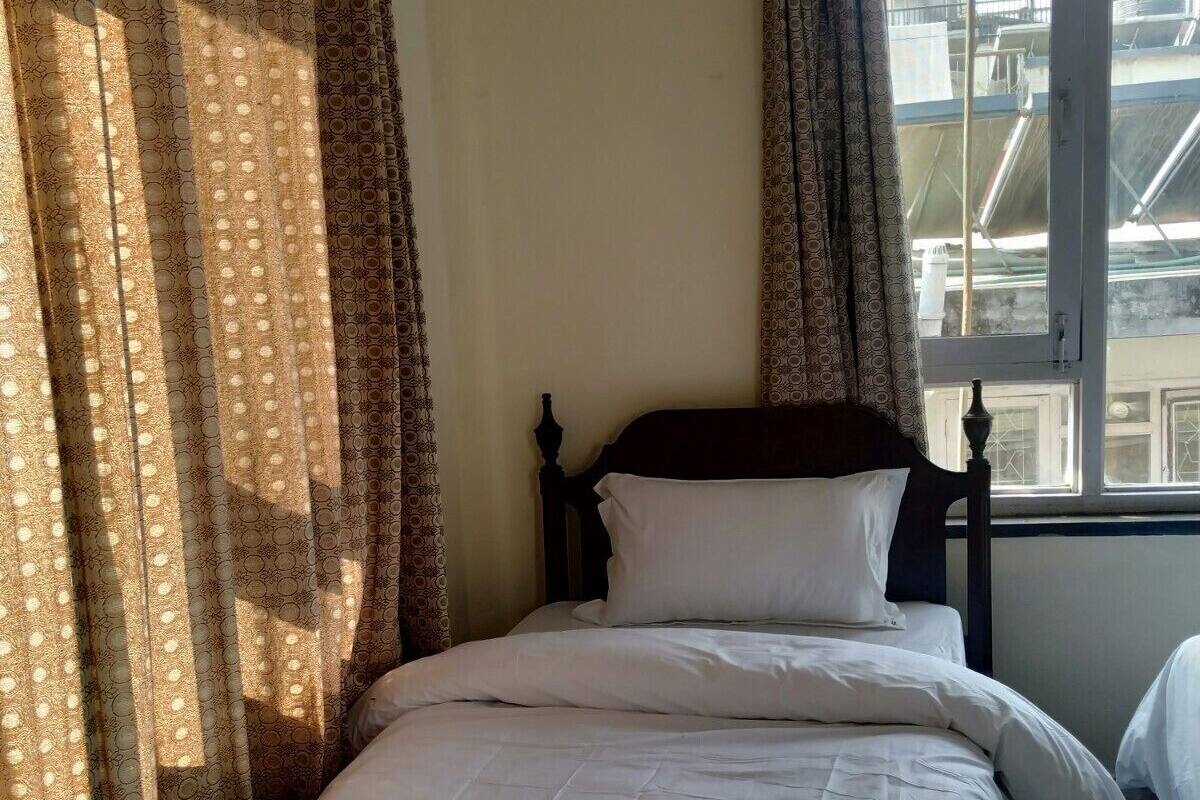A single bed with white bedding in a room with a window and patterned curtains.