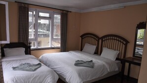 Une chambre avec deux lits simples, une tête de lit en bois, une petite table et une fenêtre avec des rideaux.