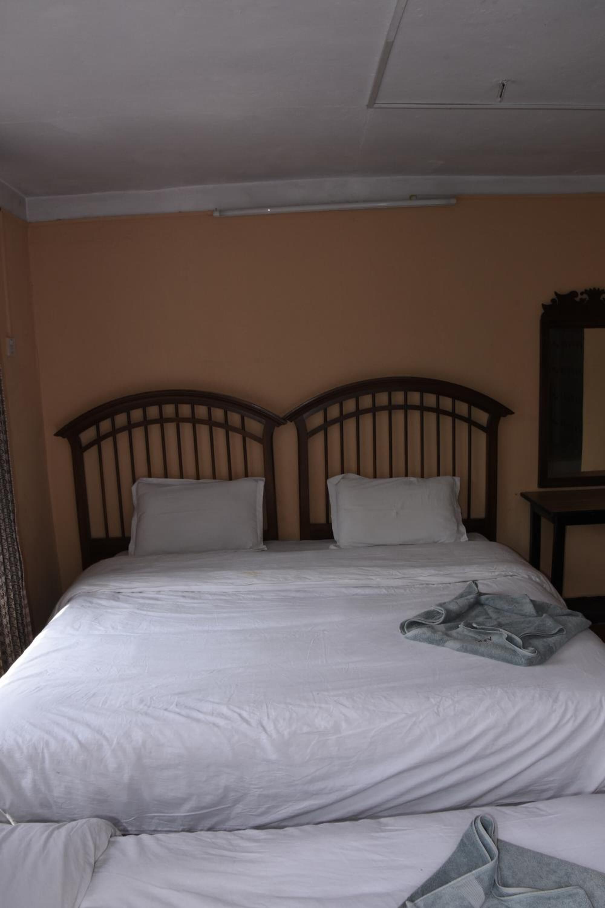 A single bed with a wooden headboard, white bedding, and a small table with a mirror to the right.