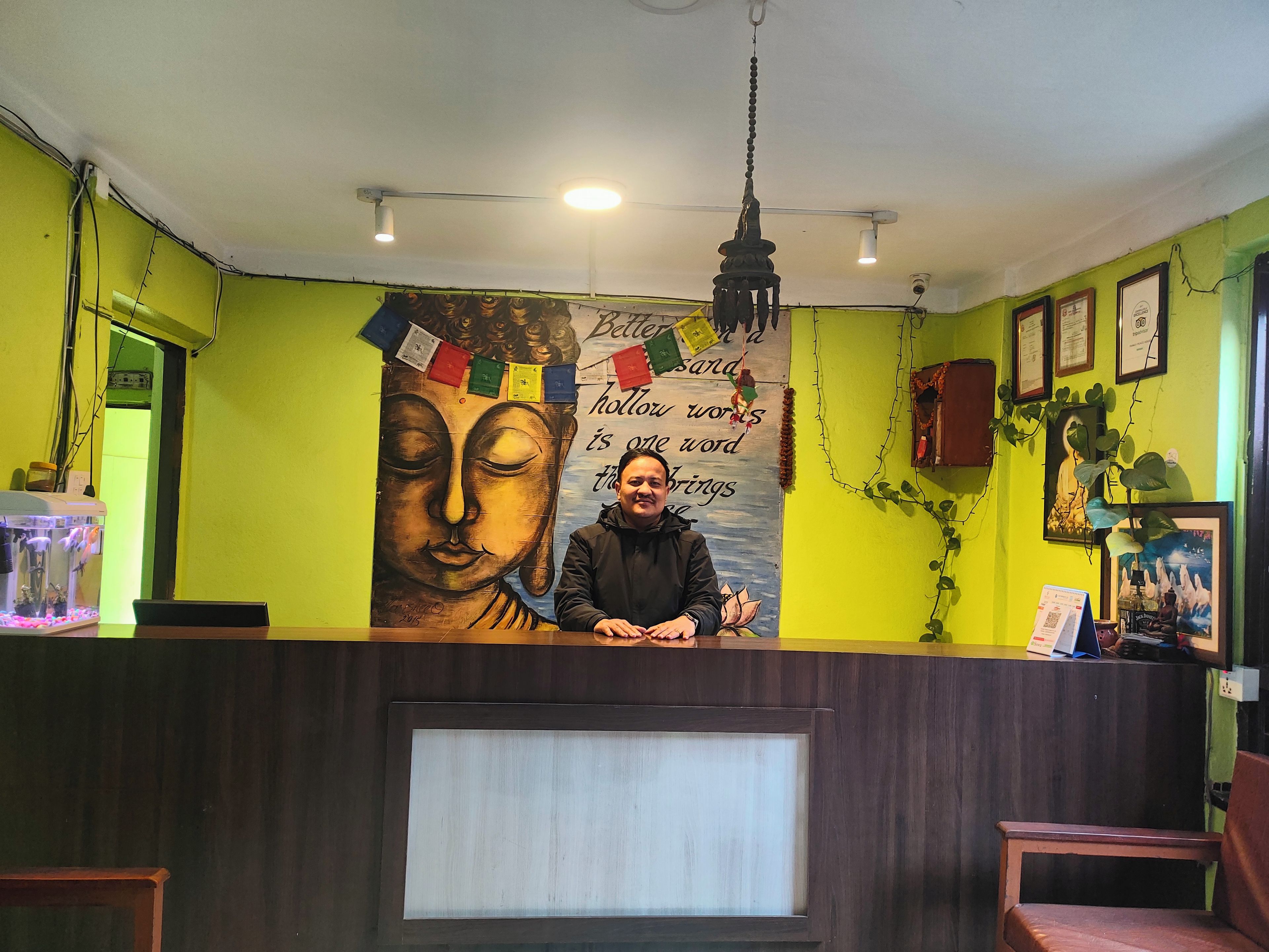 Un comptoir d’accueil orné d’une fresque représentant un Bouddha, un ventilateur de plafond et une citation encadrée accrochée au mur.