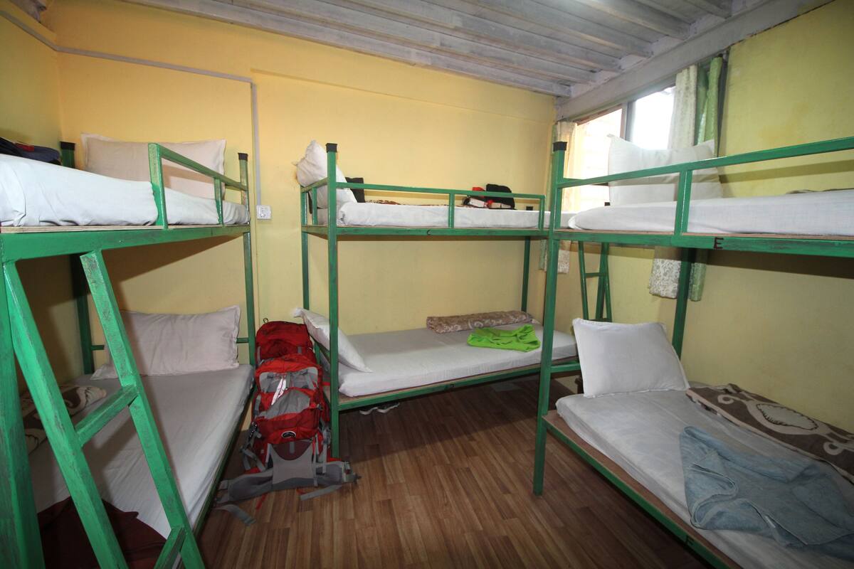 A dormitory room with bunk beds, wooden flooring, and a window with curtains.
