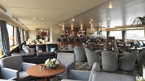 Ein großzügiger Lounge-Bereich mit verschiedenen Sitzgelegenheiten, einer Bar und Blick auf das Deck.