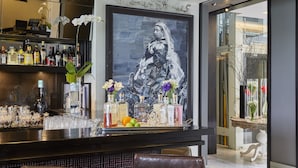 A bar area with a large painting, various liquor bottles, and decorative flowers.