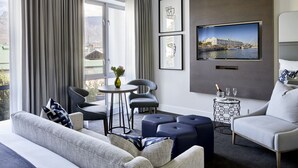 A modern living room with a sofa, chairs, a small table, and a TV mounted on the wall.