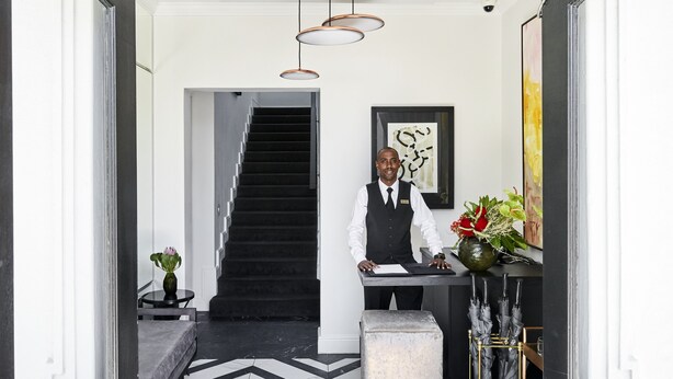 A hotel reception area with a modern staircase, a reception desk, and a vase with flowers.