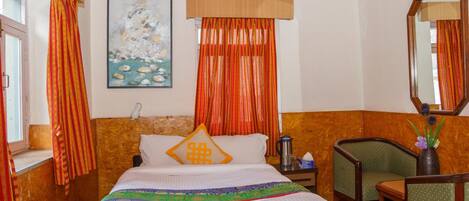 Una habitación de hotel con cama, sillón, mesa, espejo y un cuadro en la pared.