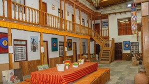 A spacious room with a wooden bench, a dining table with a red tablecloth, and a staircase leading to an upper level. - Hotel Om's Home (Jomsom)