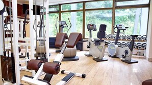 Uma academia com equipamentos de cardio, aparelhos de musculação e um painel com halteres empilhados.
