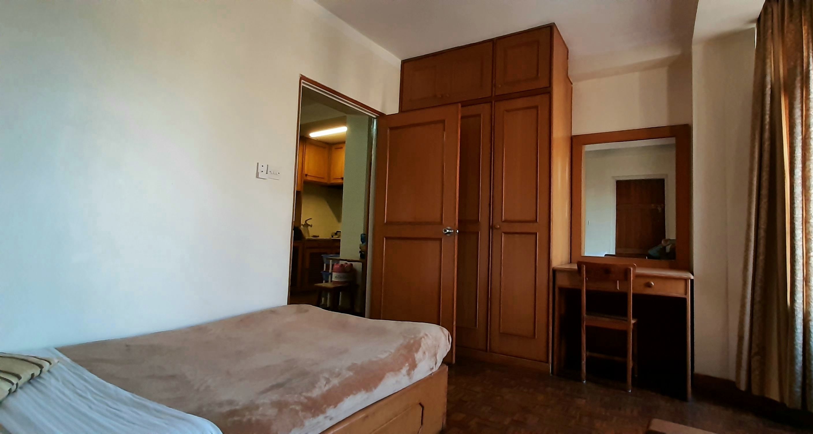 A bedroom with a bed, wooden wardrobe, a desk with a chair, and a mirror.