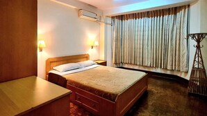 Una habitación de hotel con cama, mesitas de noche, ventilador de techo, aire acondicionado y ventana con cortinas.