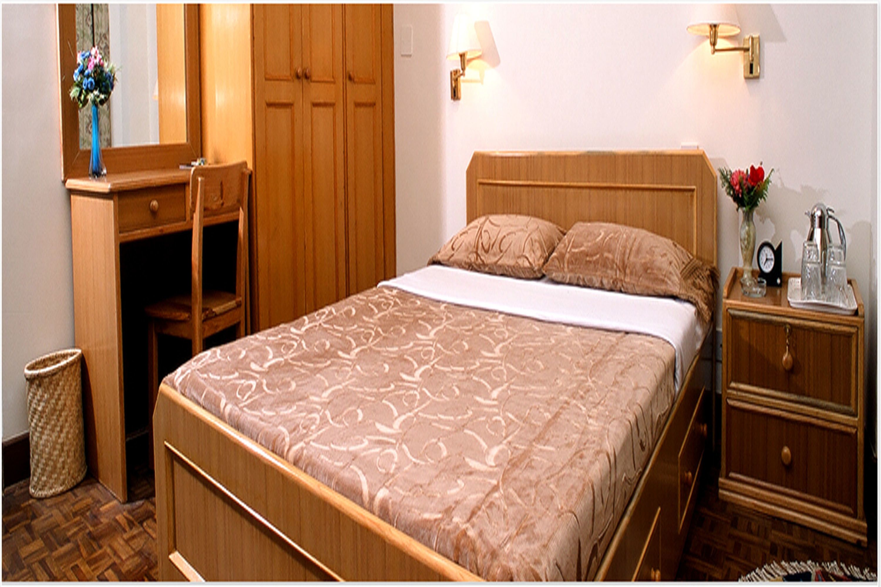 A neatly arranged bedroom with a wooden bed, a nightstand with a clock, a dresser, and a mirror.